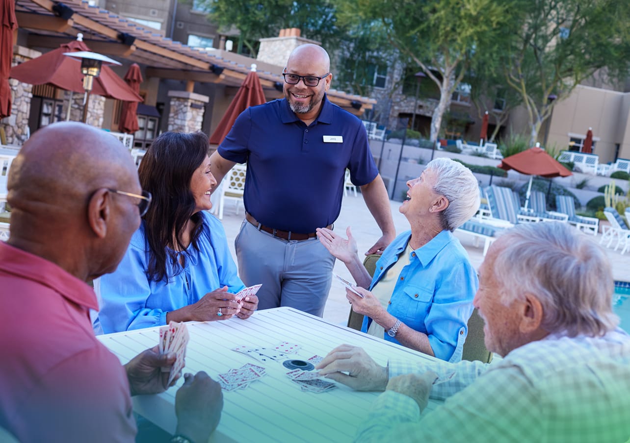 staff member visiting with a group of residents playing cards at a picnic table